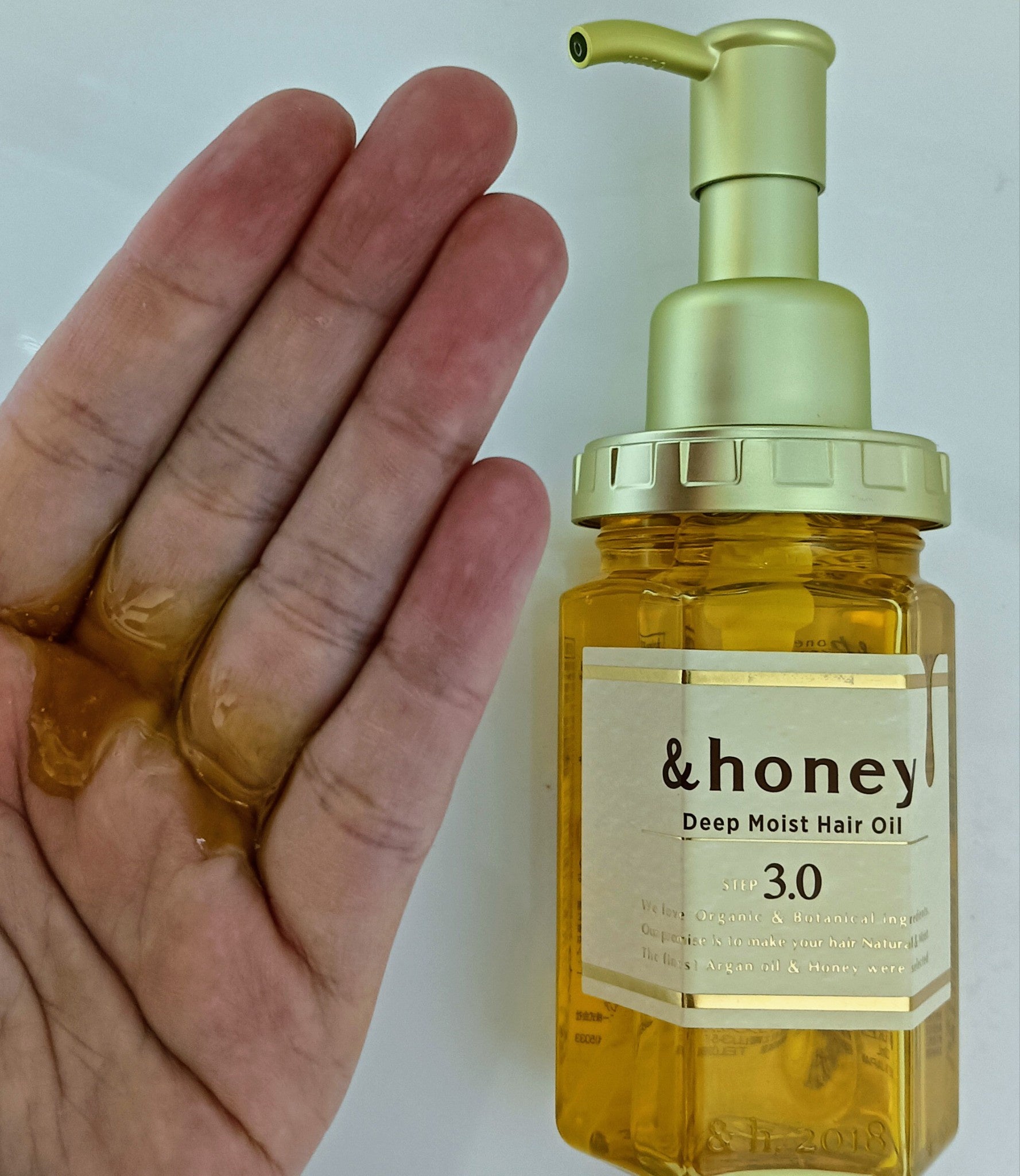 &honey Deep Moist 3.0: botella junto a una mano con una muestra de aceite.